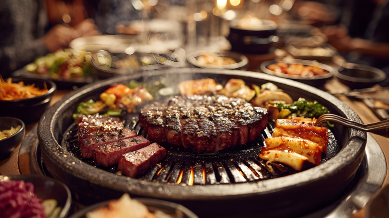 Korean BBQ with sizzling grilled meat, vegetables, and flames on a tabletop grill, surrounded by side dishes