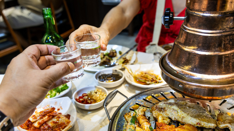 Two people toasting soju drinks during dinner in a Korean barbecue restaurant
