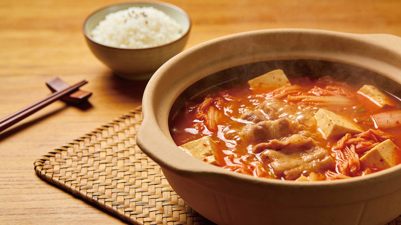 A bowl of Kimchi Jjigae with tofu and pork and a bowl of rice
