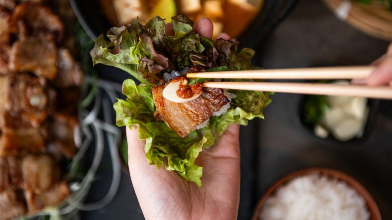 Hand preparing Korean pork belly ssam with chopsticks