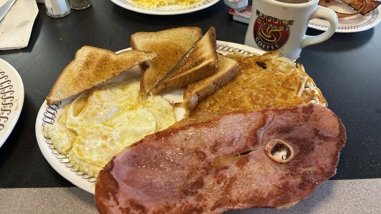 A plate of Waffle House ham with eggs over easy, toast, hash browns and a cup of coffee.