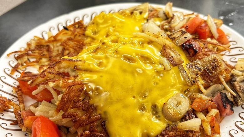 A plate of Waffle House Hash Browns covered in cheese, onions and tomatoes.