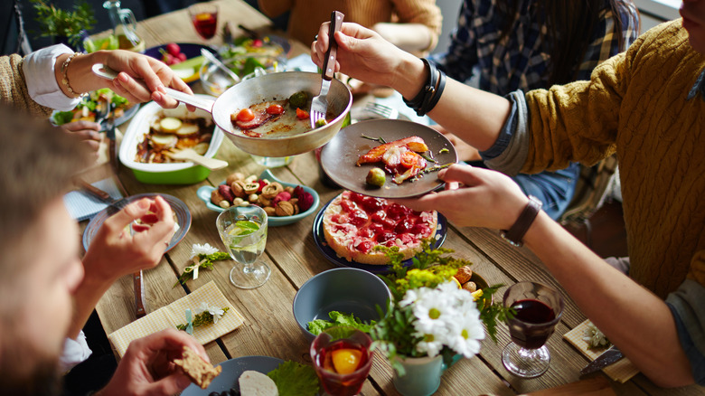 People sitting at a dining table and eating dishes family-style