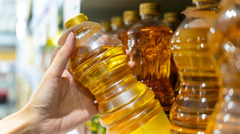 Woman's hand shown selecting bottle of oil from a shelf in a supermarket