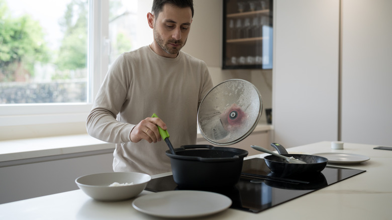 Man lifting the lid off a pot while cooking rice on an induction stove in a modern kitchen