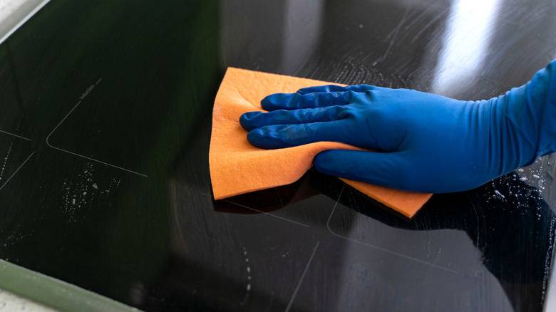 Hand in blue glove washing an induction cooktop with a sponge