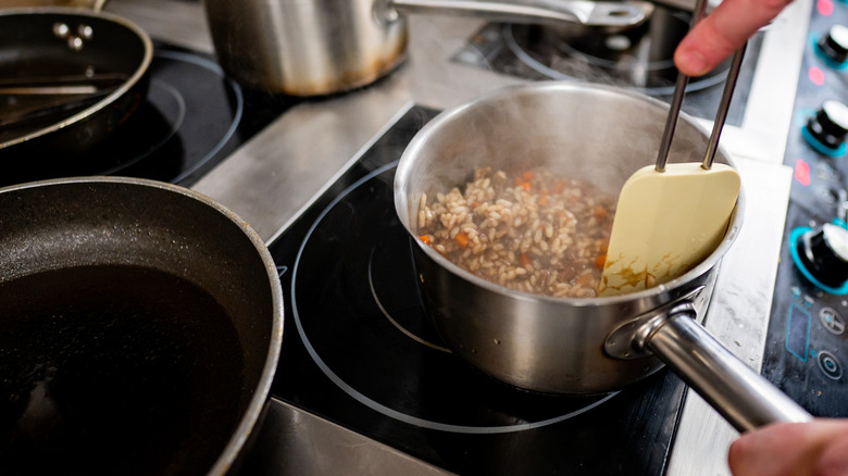 A cook using a spatula and chopsticks to stir a pot on an induction stove