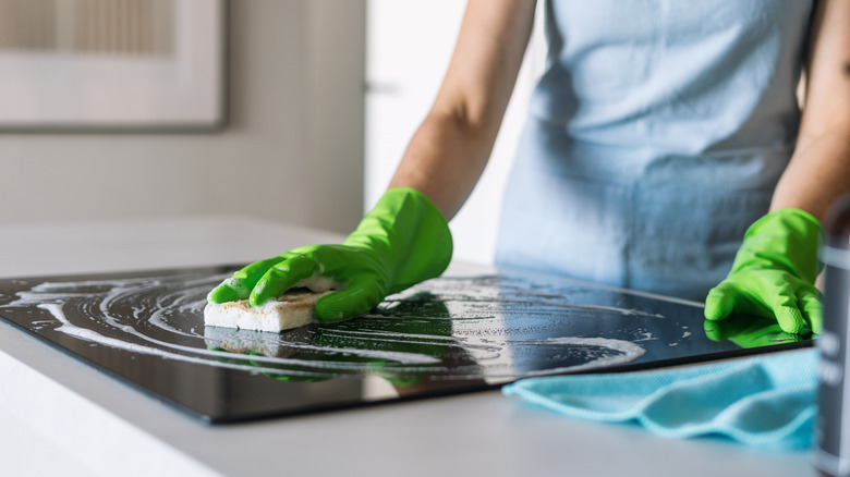 Person in green gloves cleans a sleek induction stove with a sponge