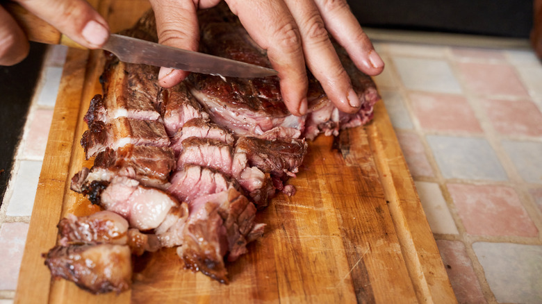 Man holding steak on cutting board with one hand and slicing with knife with the other hand