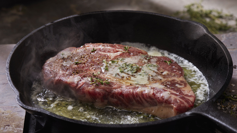 Basting steak with butter and herbs in cast iron pan
