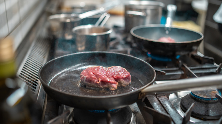 Close up of in raw steak cooking in pan on gas burners in kitchen