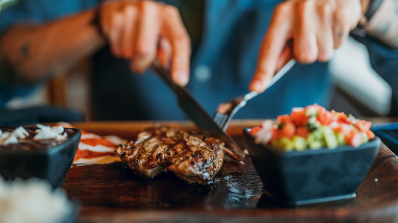 Close up of man cutting into steak with fork and knife