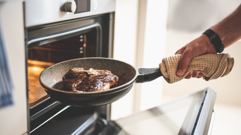 Man using dish towel to remove frying pan with steak from oven