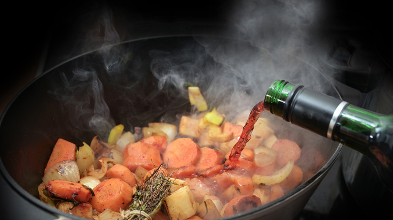 Meat and vegetables being deglazed with red wine