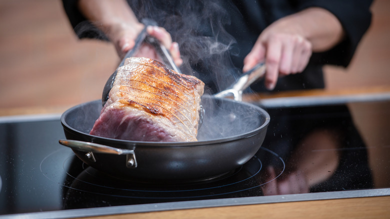 A roast being seared in a black pan