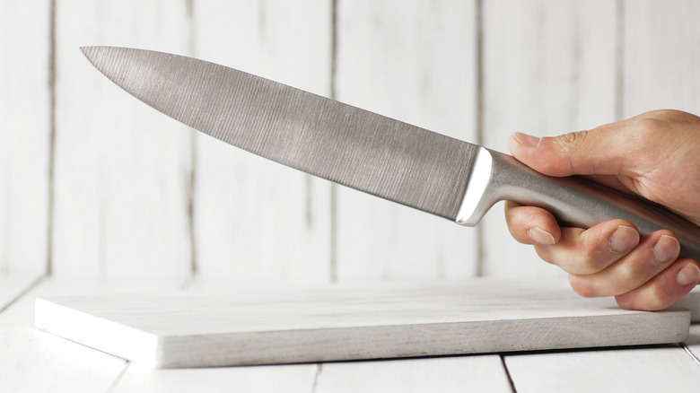 A hand holding a chefs knife above a cutting board