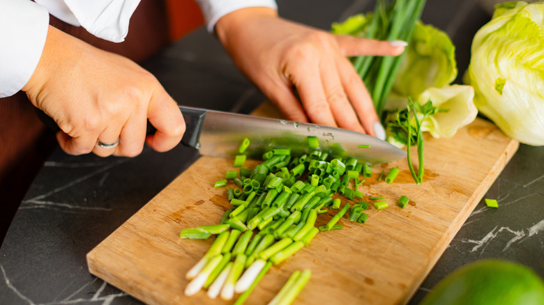 Person slicing green onions with a knife on a cutting board