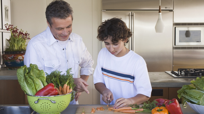 Man and young boy slicing carrots in home kitchen