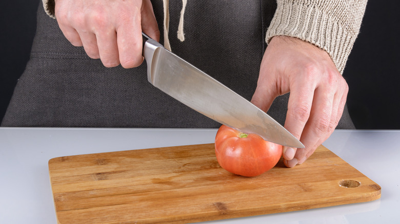A tomato being sliced with a chefs knife on a wooden board