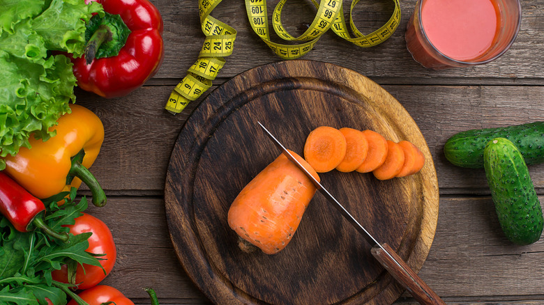 Chopped and whole vegetables on a wooden board next to a tape measure