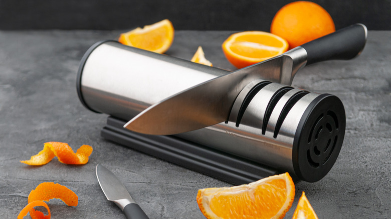 An electric knife sharpener and knife surrounded by cut pieces or orange