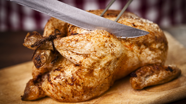 A whole roasted chicken about to be carved with a sharp knife and a fork