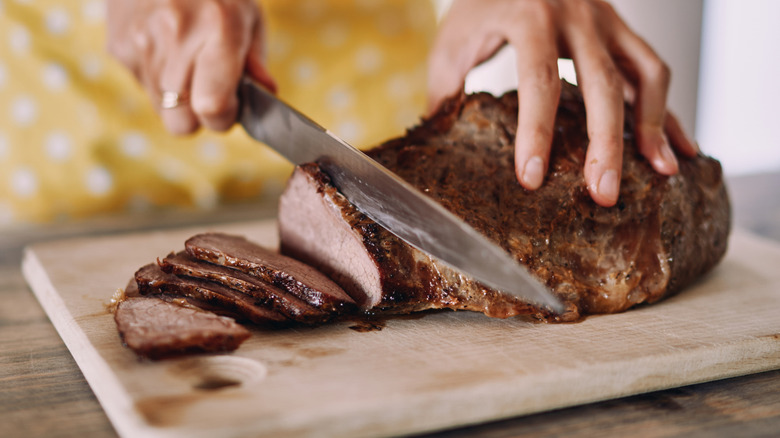 Hands carving a roasted piece of meat with a sharp knife on a cutting board