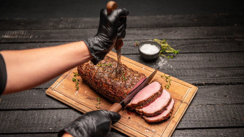 A chef uses a sharp knife to slice a cooked roast on a wooden board