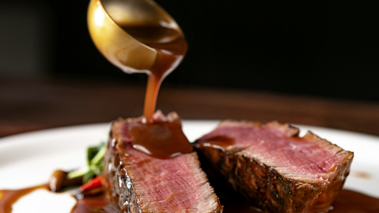 Sauce being poured from a ladle onto a plate of sliced steak