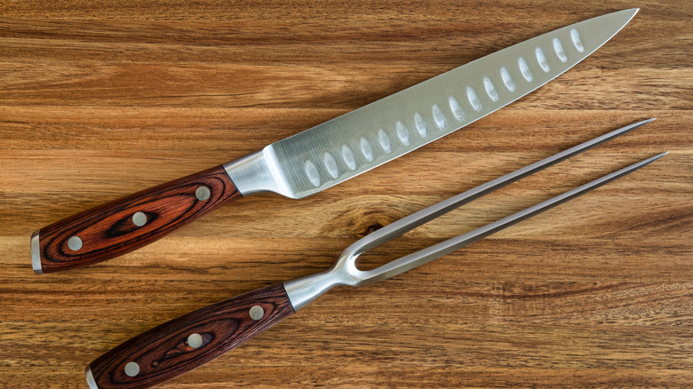 A carving knife and fork set on a wood cutting board