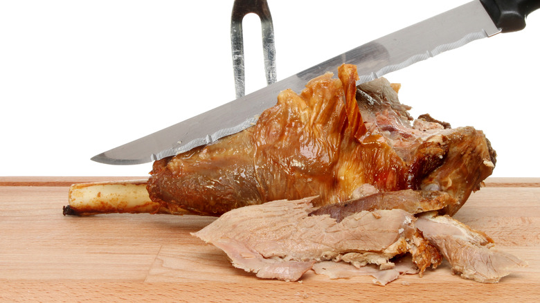 A roast leg of lamb joint being carved on a wooden board
