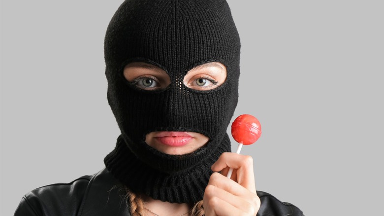 Person wearing a black mask holding a lollipop