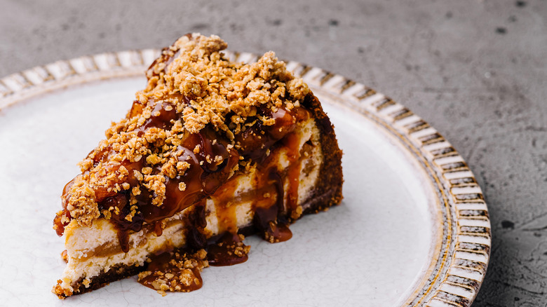 Single slice of rich caramel cheesecake topped with crushed nuts, presented on an elegant plate