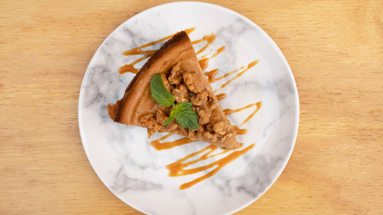 Top view of a slice of dulce de leche cheesecake with walnuts and caramel sauce in a marble dish on wood.