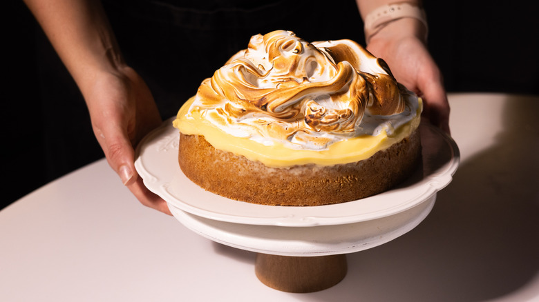 Lemon cheesecake with lemon curd and burnt meringue, being placed on a cake stand