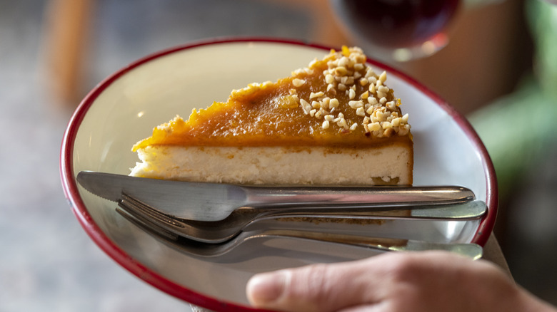 close-up of a hand holding a plate with a slice of pumpkin cheesecake with chopped nuts