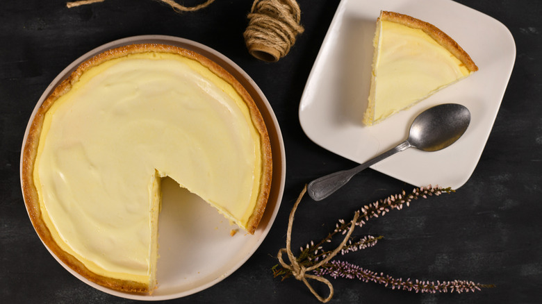 Traditional New York cheesecake with cream cheese and sour cream layer with one slice on white plate