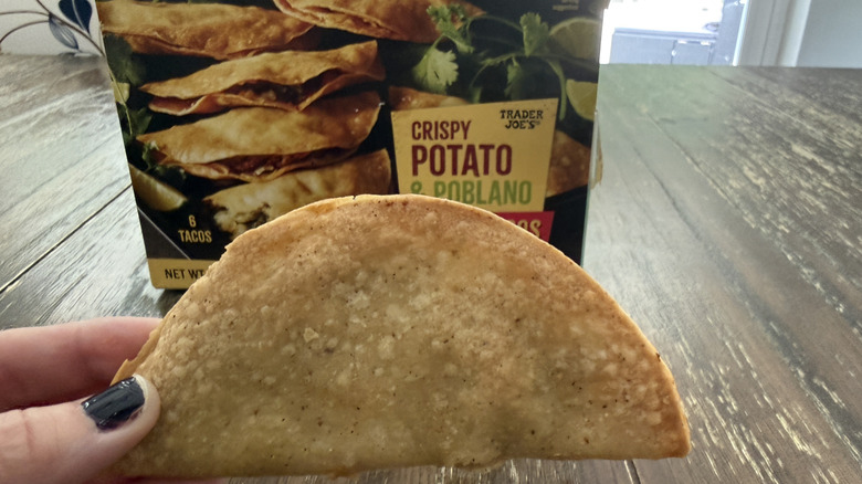 Package of Trader Joe's crispy potato and poblano tacos on wooden table with one being held by a hand