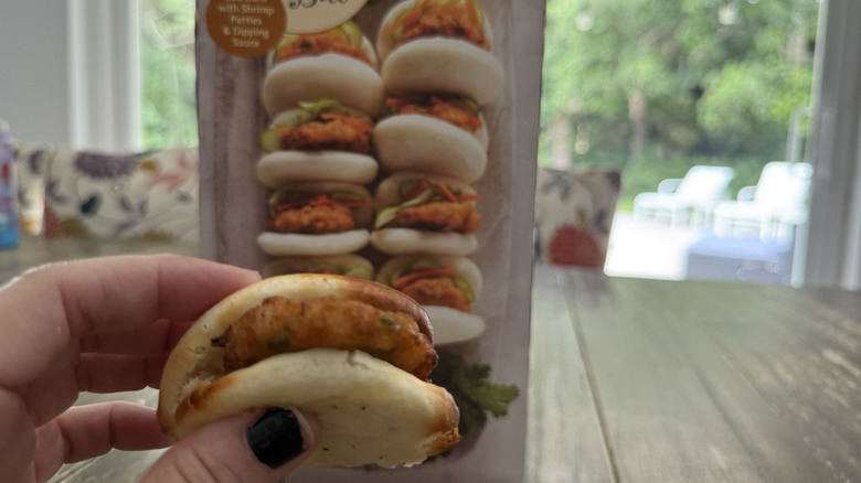 Package of Trader Joe's mini shrimp bao on wooden table and one held by a hand