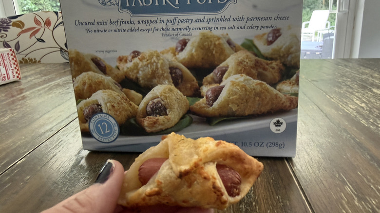 Package of Trader Joe's pastry pups on wooden table and one held in a hand