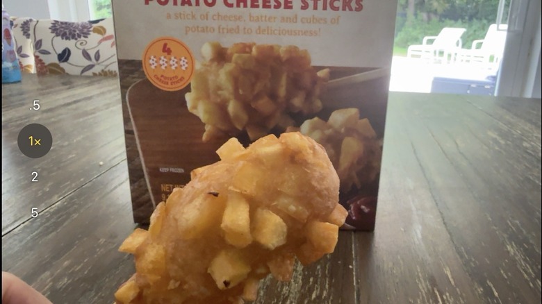 Package of Trader Joe's crispy potato cheese sticks on wooden table and one held by a hand