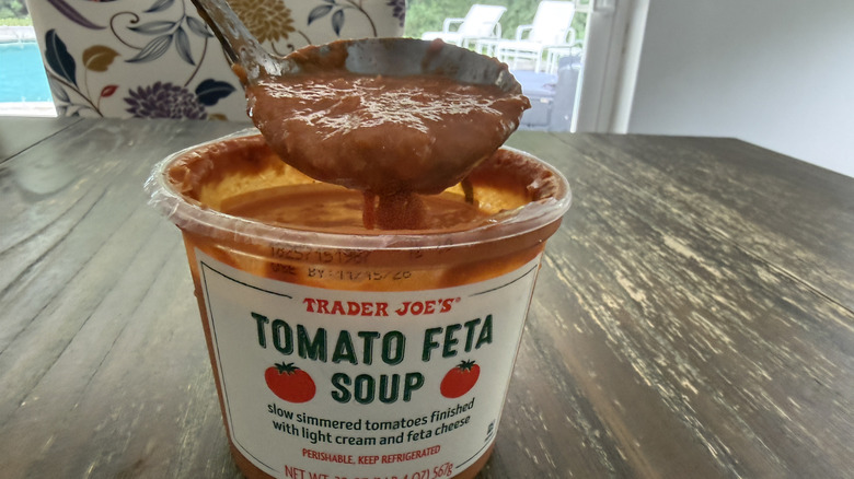 Trader Joe's tomato feta soup on wooden table with a spoon scooping a bite out of it