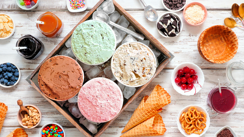 Top view of open pints of ice cream on ice surrounded by small bowls of assorted toppings