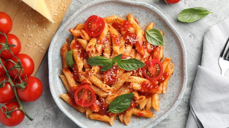 a plate of penne pasta with tomato sauce, topped with sliced tomatoes and basil