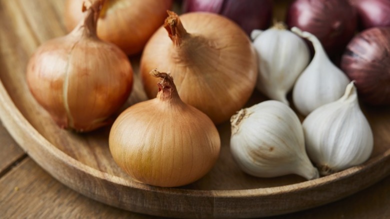 a wooden plate holding yellow and red onions and garlic