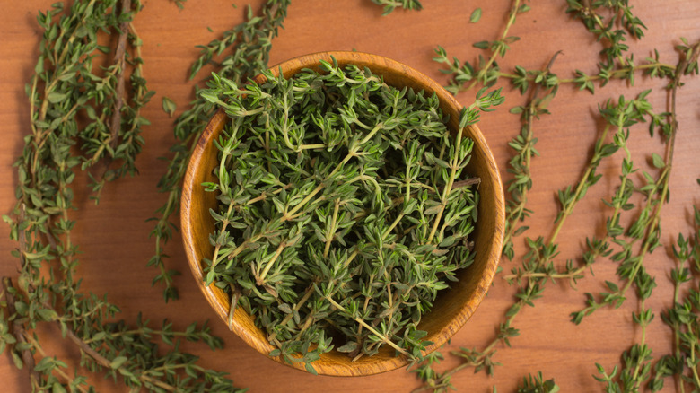 Fresh thyme in wooden bowl on wooden surface scattered with sprigs of fresh thyme