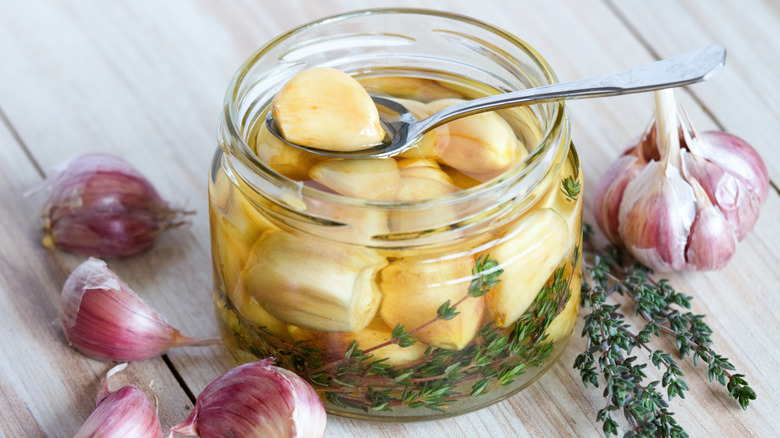 Spoon with clove of garlic balanced on glass jar of pickled garlic and thyme sprigs