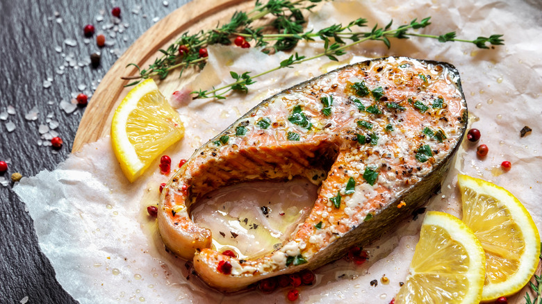 Fried salmon steak with thyme and lemon served on wooden plate on table.