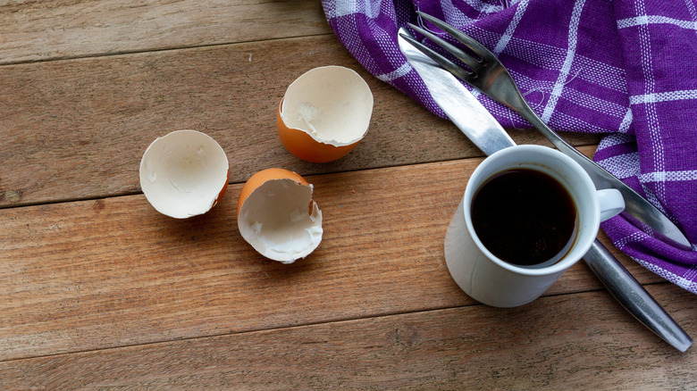 Eggshells beside a cup of coffee and fork and knife