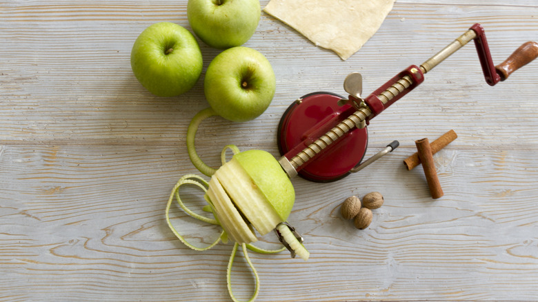 A green apple being peeled by an apple peeling machine surrounded by green apples